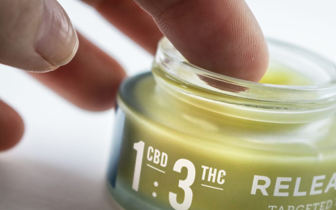 person dips a finger into a pot of cbd topical ointment